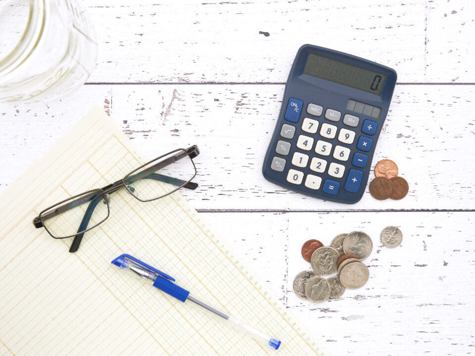 A notepad, calculator and coins on a desk